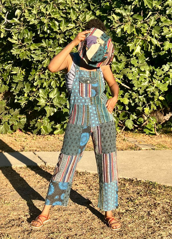 Front view of handmade blue patchwork cotton overalls worn outdoors styled with hat