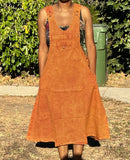 Model standing outdoors in burnt orange cotton overall dress with hands in pockets