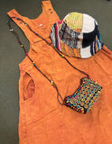 Handmade burnt orange cotton overall dress laid flat with hat and purse for styling inspiration