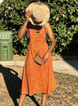 Model wearing burnt orange cotton overall dress with hat and purse to show styling options