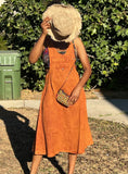 Model wearing burnt orange cotton overall dress with hat and purse to show styling options